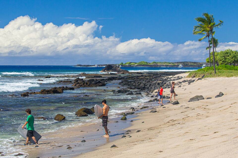 A beach with rocky shoreline, palm trees, and ocean waves.