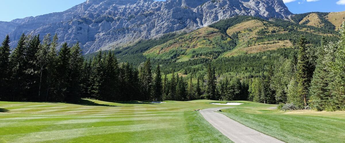 Gorgeous par 4 on a golf course surrounded by forest and big mountains in the background, on a beautiful sunny day in Kananaskis, Alberta, Canada.