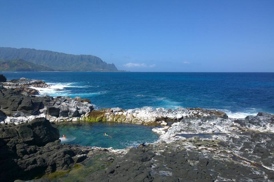 A rocky coastline with clear blue waters and distant mountains.