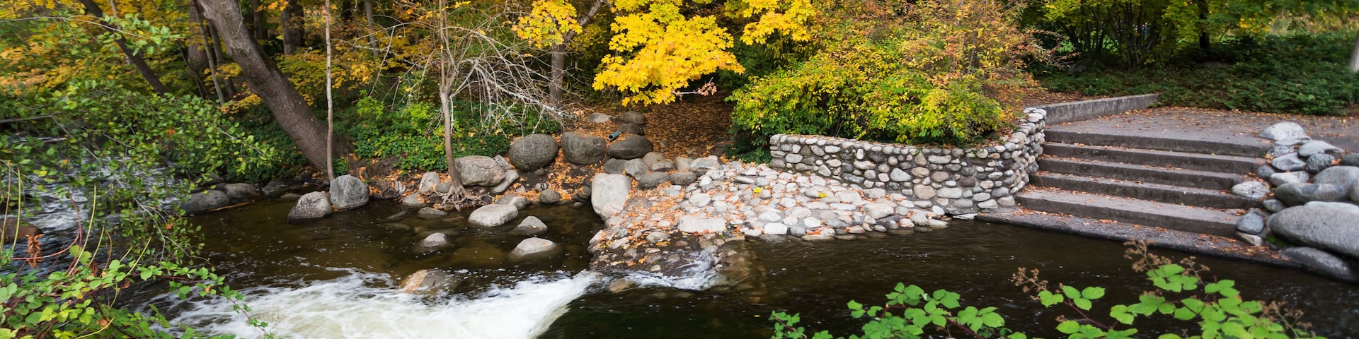 Un arroyo serpenteando sobre rocas con un puente de piedra y follaje otoñal.