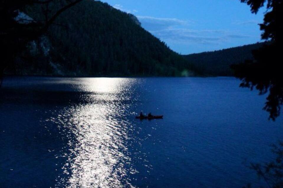 Un lago sereno al anochecer con un bote en primer plano y una montaña al fondo.