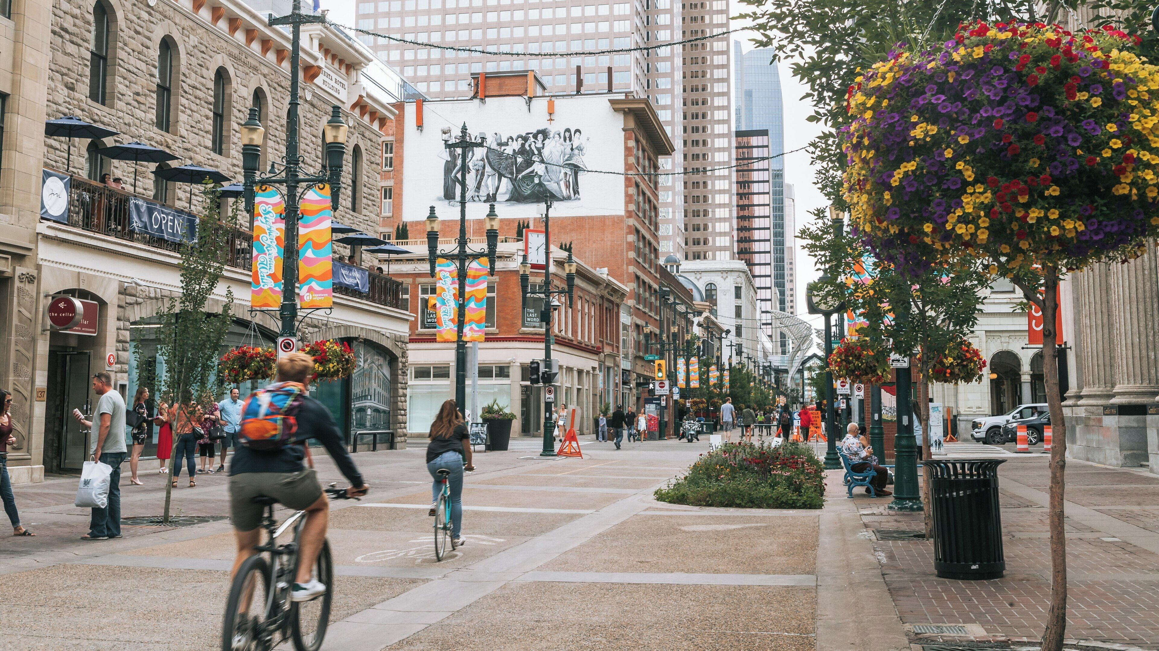 Busy Stephen Avenue in Downtown Calgary showcases cyclists, pedestrians, and vibrant storefronts on a sunny day in Alberta, Canada