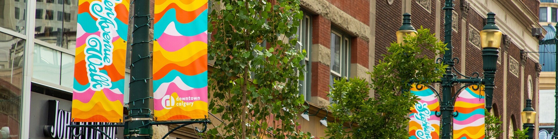 Banderines coloridos colgados de un poste de luz, un cesto de flores y un edificio con un letrero que dice "downtown calgary".
