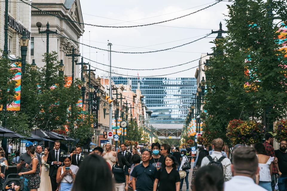 A busy urban street lined with historic buildings, a modern glass skyscraper, and decorative string lights.