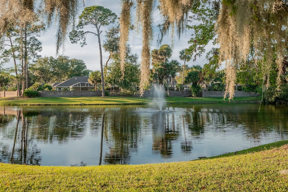A pond with a fountain, surrounded by trees and a house.