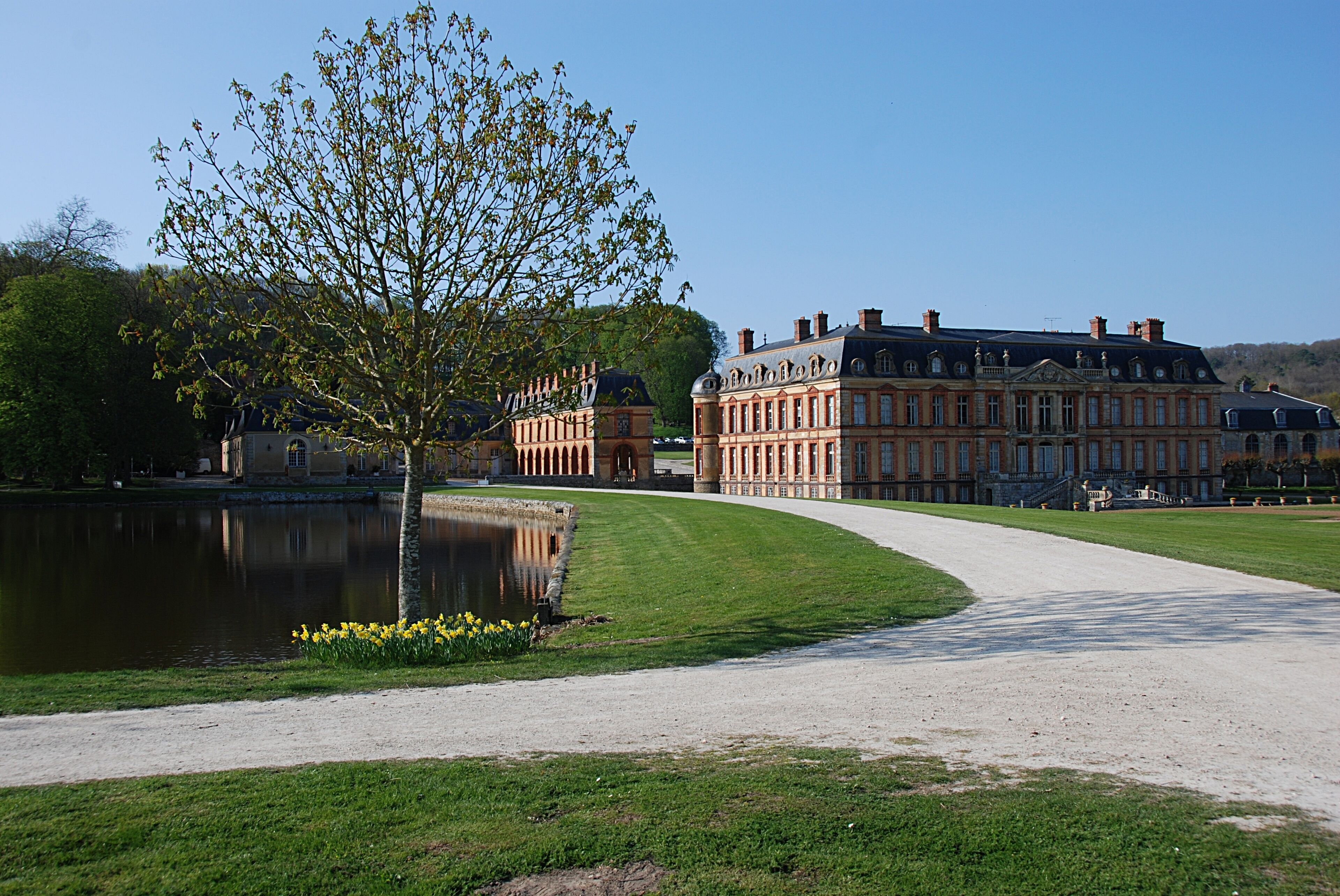 A large classical building with a pond and a tree in a park.
