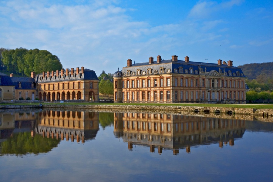 Ein historisches Gebäude mit Spiegelung im Wasser, umgeben von Grünflächen und Hügeln.