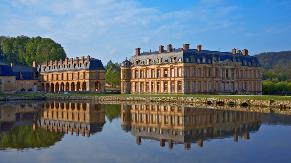 A historic building with a reflection in the water, surrounded by greenery and hills.