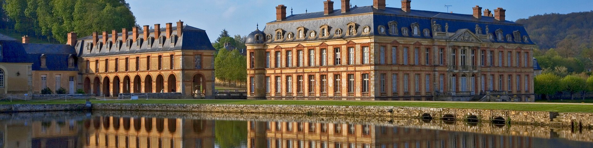 Un bâtiment historique qui se reflète dans l’eau, entouré de verdure et de collines.