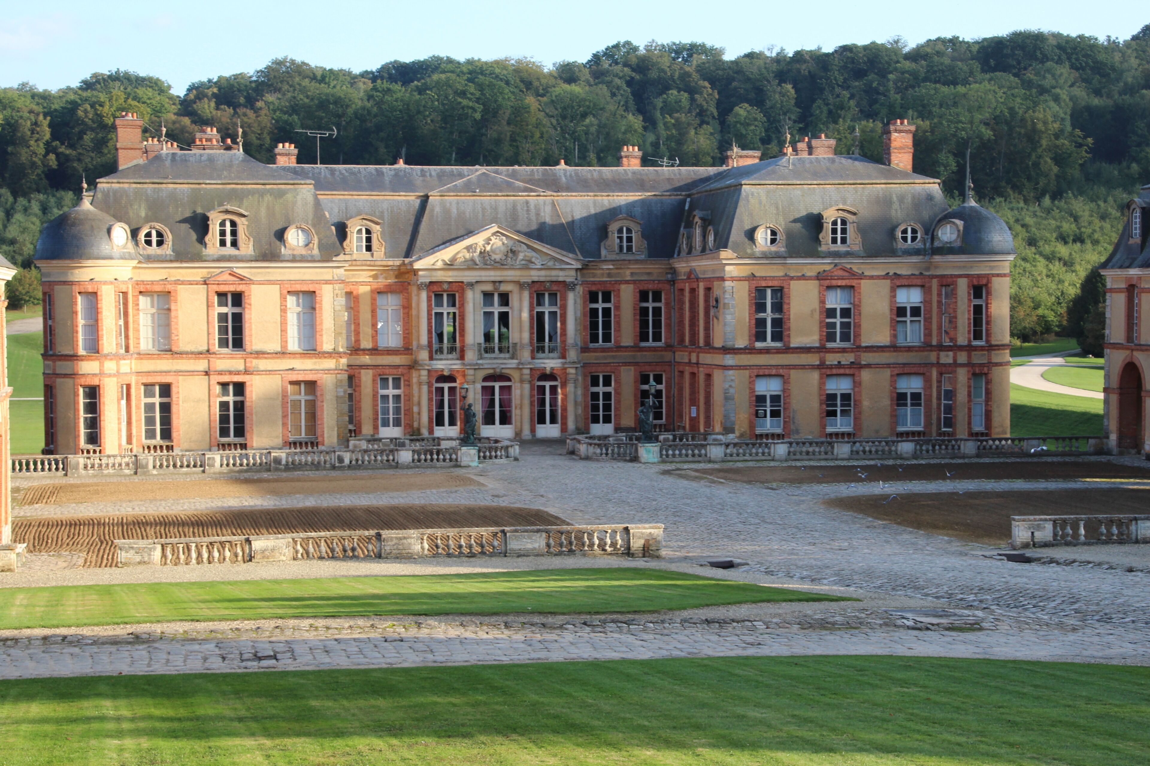 A large, historic building with a symmetrical facade, surrounded by a well-maintained lawn and a cobblestone courtyard.