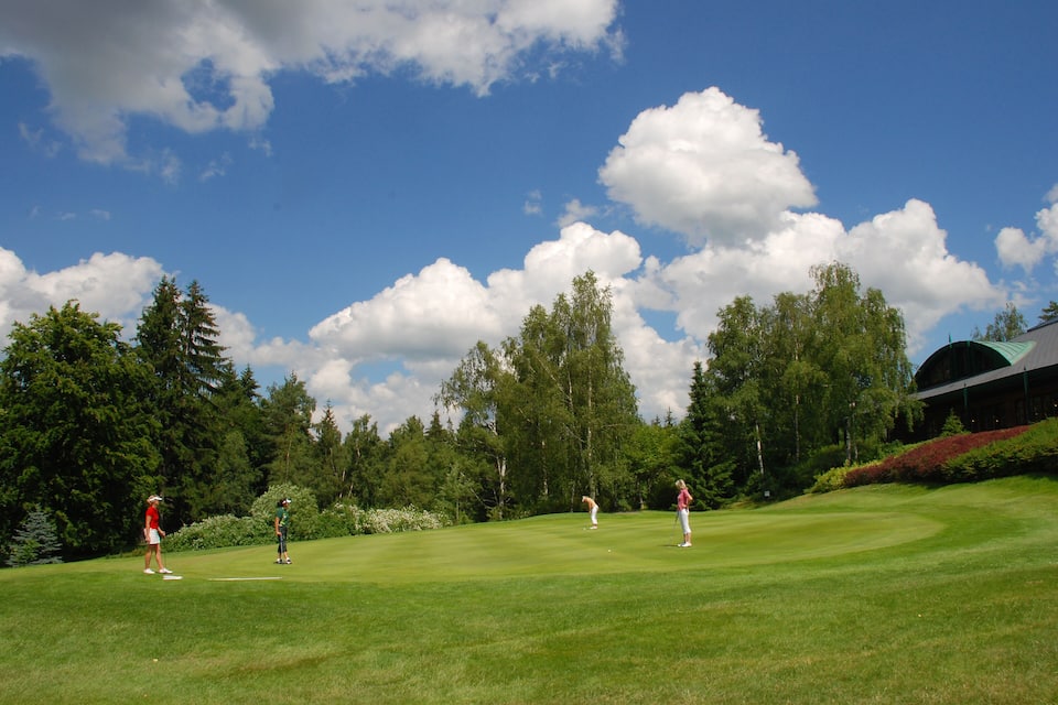 Een golfbaan met spelers, bomen en een gebouw op de achtergrond.