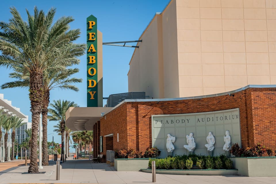 A building with a sign reading "PEABODY AUDITORIUM" and palm trees in the foreground.