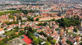 Eine Vogelperspektive auf eine dicht bebautes Stadtbild mit historischer Architektur, darunter eine markante Kirche mit einem hohen Turm und ein schlossartiges Gebäude.