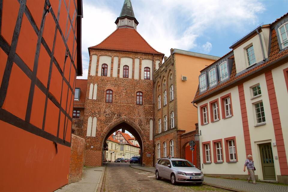 Una calle estrecha con edificios históricos, incluyendo una imponente torre de ladrillo con techo puntiagudo y un arco.