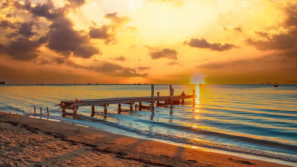 A sunset over a calm sea with a pier extending into the water.