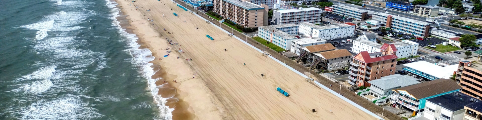 Paisagem costeira com uma extensa praia de areia, edifícios altos adjacentes e vista para o oceano.