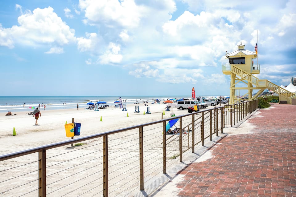 A beach with a lifeguard tower, umbrellas, and a brick walkway.