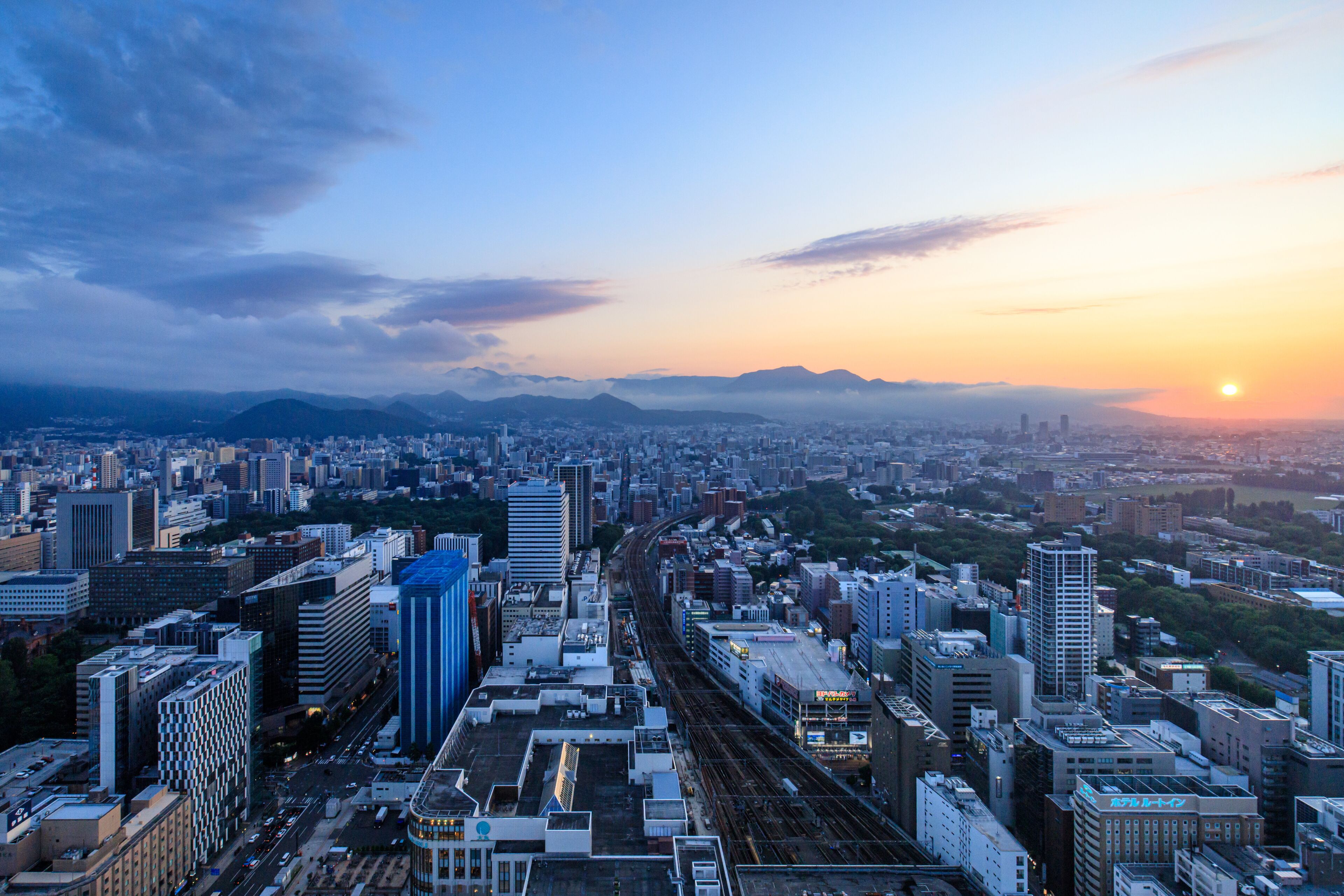 A cityscape with a sunset, high-rise buildings, and a train track.