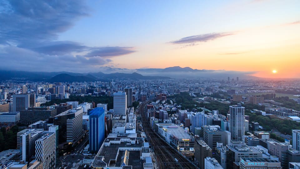 A cityscape with a sunset, high-rise buildings, and a train track.