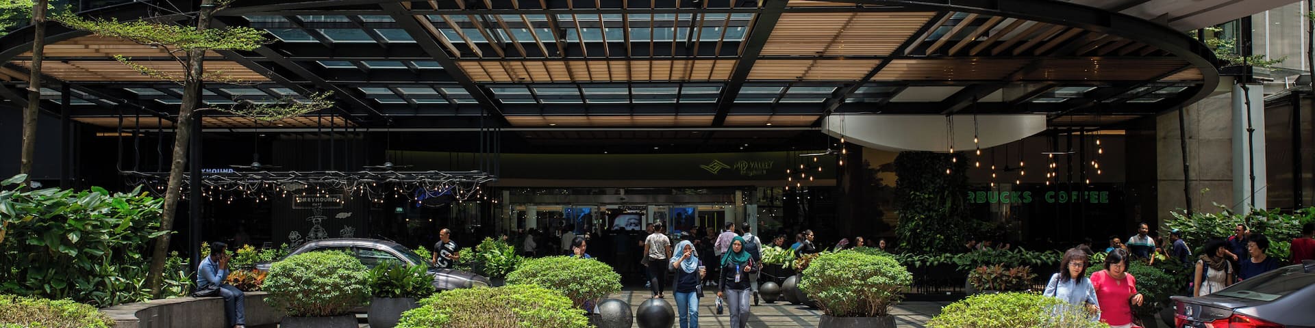 A modern building with a glass facade, large potted plants, and a covered entrance.