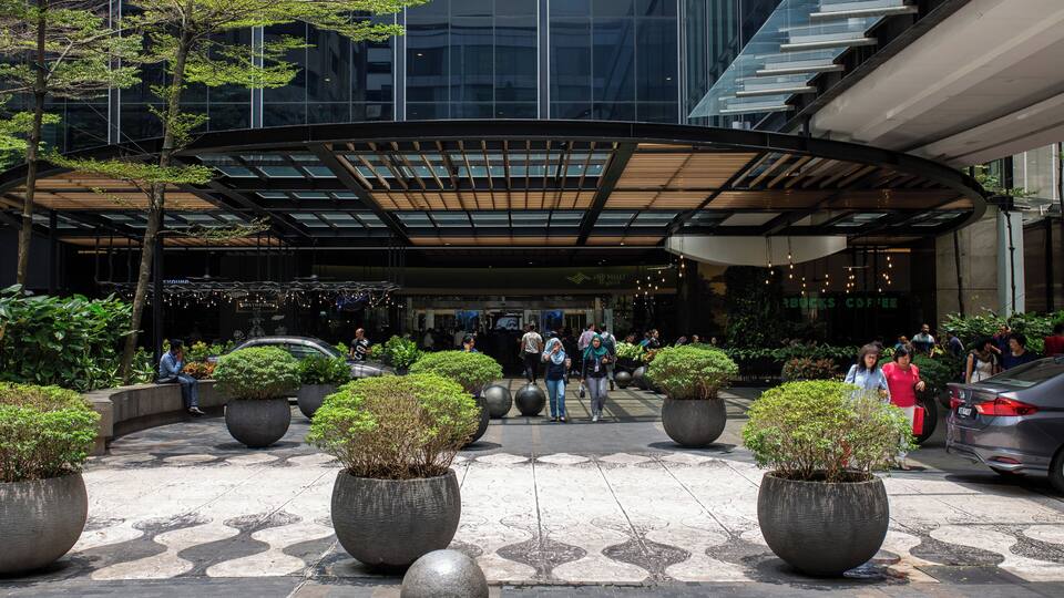 A modern building with a glass facade, large potted plants, and a covered entrance.