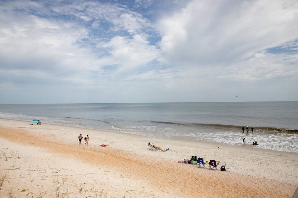 A sandy beach with people, a few beach chairs, and a calm sea under a partly cloudy sky.