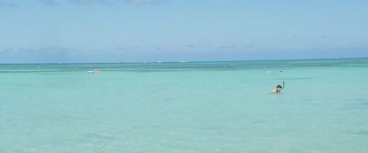 A clear blue sea with a few people swimming.