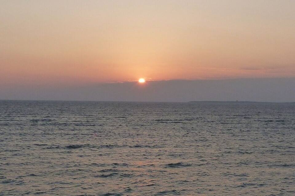 A sunset over the ocean with people on the beach.