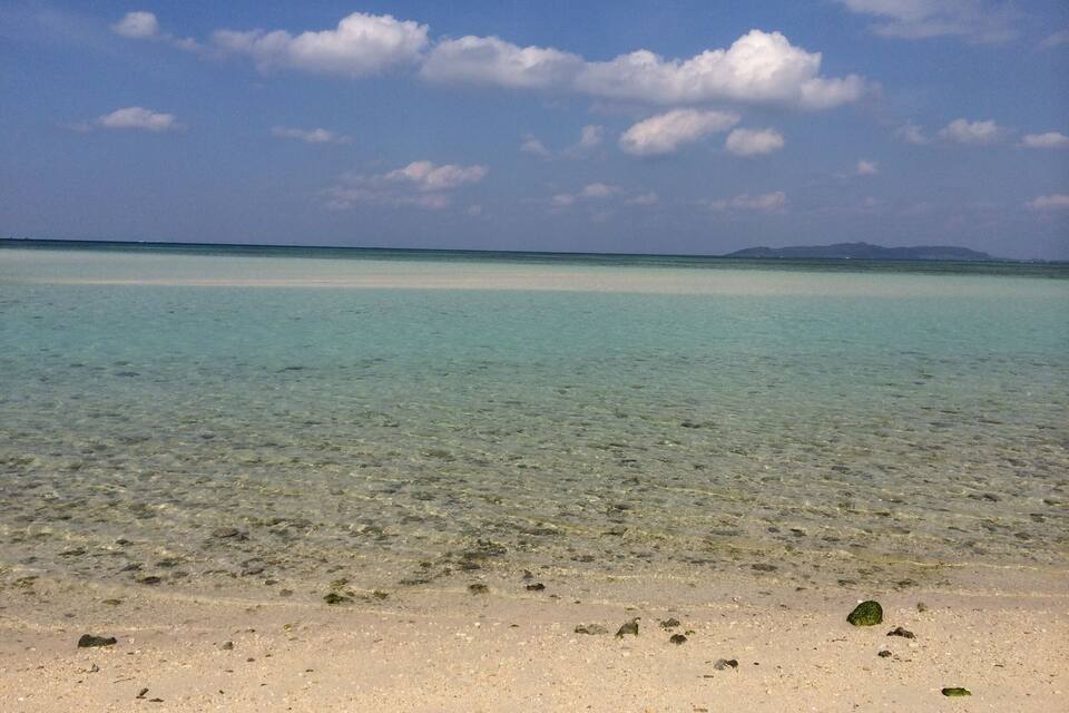 Un mar turquesa i translúcid amb una platja sorrenca i roques disperses.
