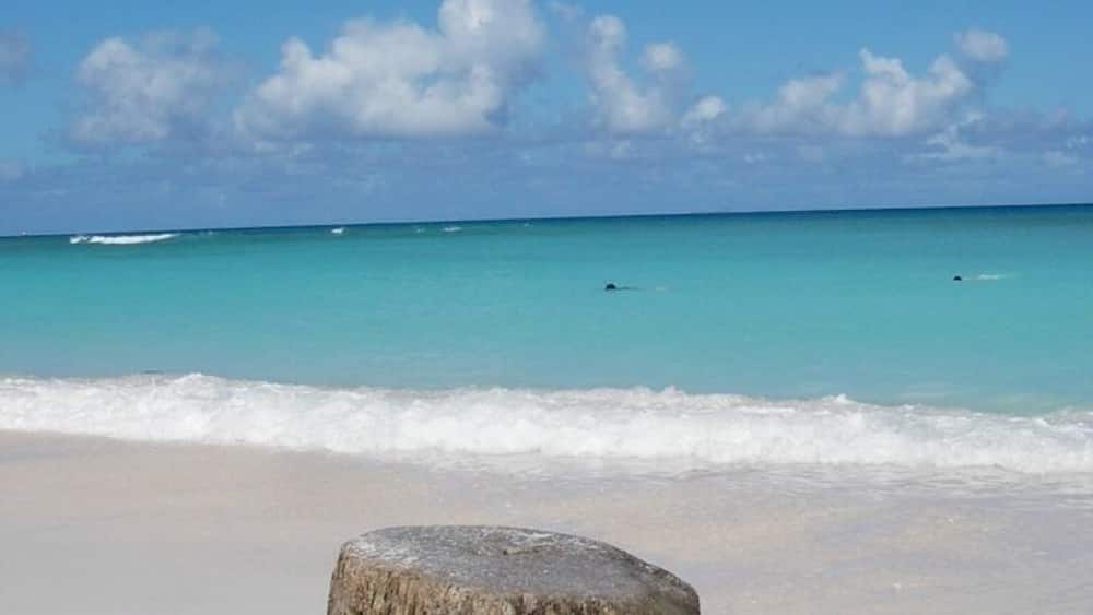 A sandy beach with a large rock in the foreground and calm turquoise waters.