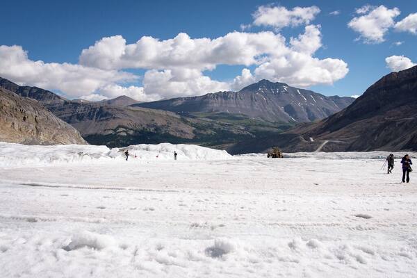 A glacier with people hiking, mountains in the background, and a clear sky.