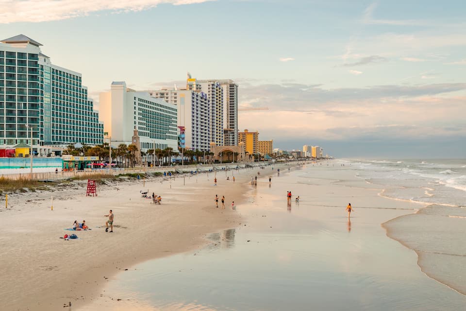 A beach with people, a boardwalk, and buildings in the background.