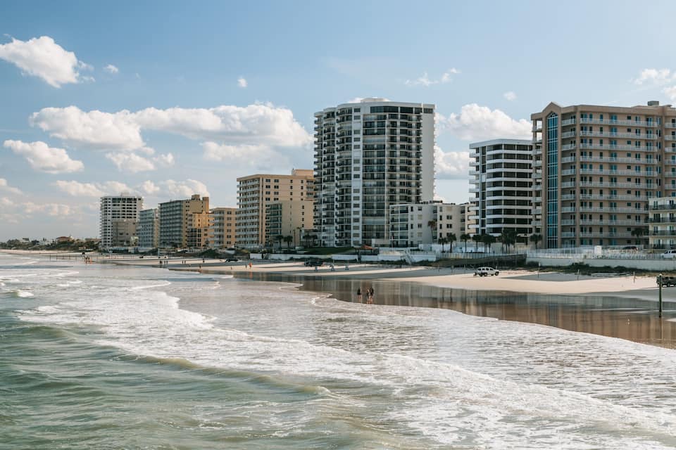 A beach with waves, a sandy shore, and several high-rise buildings in the background.