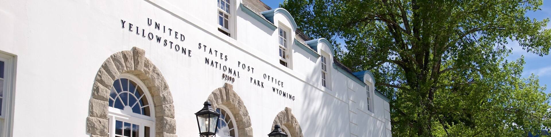A white building with stone lion statues at the entrance, labeled as the United States Post Office in Yellowstone National Park.