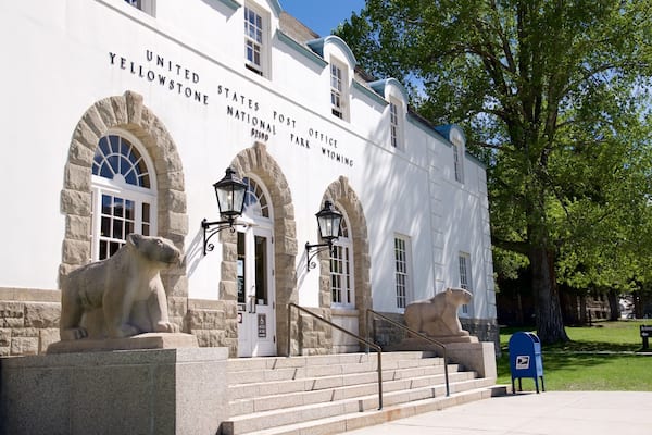A white building with stone lion statues at the entrance, labeled as the United States Post Office in Yellowstone National Park.