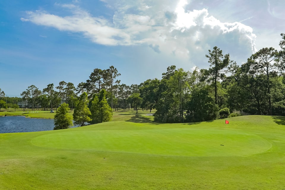 Een golfbaan met een vijver, bomen en een heldere lucht.