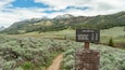 A trail sign with distances to various points: Specimen Ridge Trail (1.4 mi / 2.2 km), Cache Creek Trail (3.1 mi / 5.0 km), Miller Creek Trail (9.3 mi / 15.0 km), and Cold Creek Junction (16.7 mi / 26.9 km).
