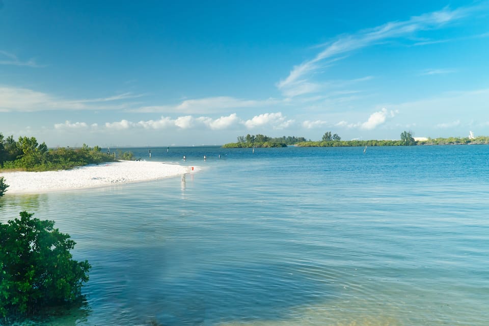 Een rustige zee met een zandstrand en een klein eiland in de verte.