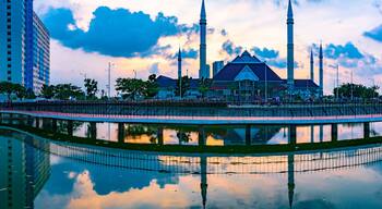 Una moschea con quattro minareti, il suo riflesso in una vasca circolare e palazzi moderni circostanti.