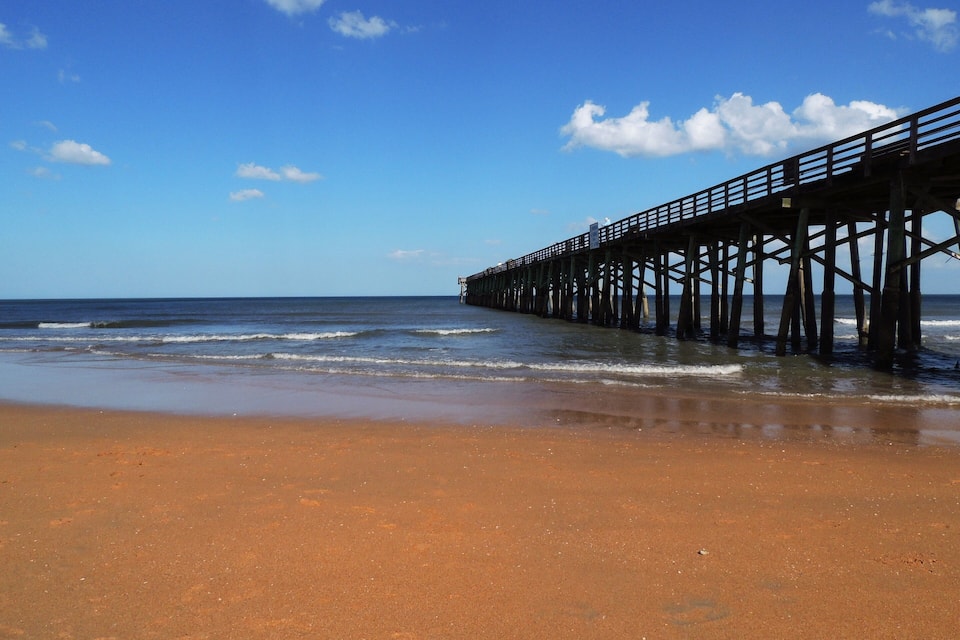 Een strand met een houten pier die zich uitstrekt over de oceaan.