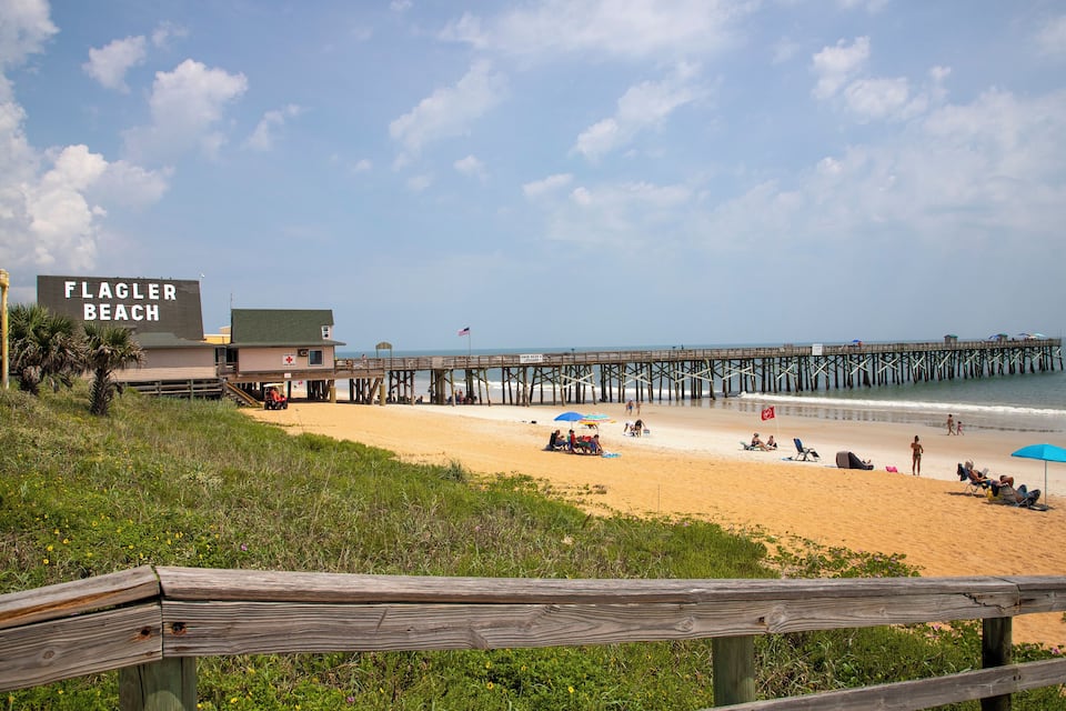 Flagler Beach con un paseo marítimo de madera, sombrillas de playa y un muelle que se adentra en el océano.