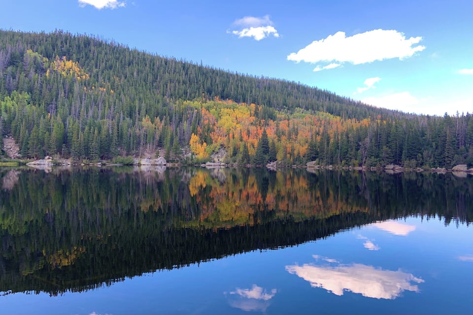 A calm lake reflecting a forest with autumn-colored trees.