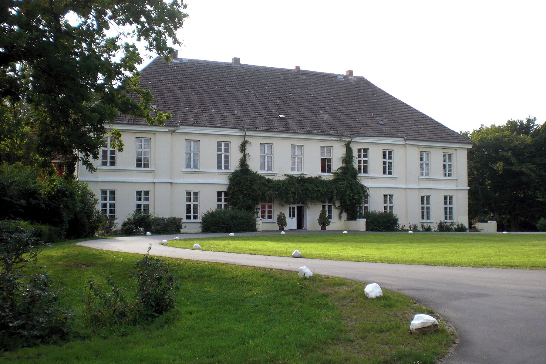 A large, two-story building with a sloped roof, surrounded by a well-maintained lawn and several trees.