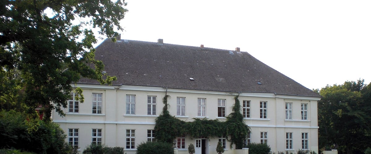 A large, two-story building with a sloped roof, surrounded by a well-maintained lawn and several trees.