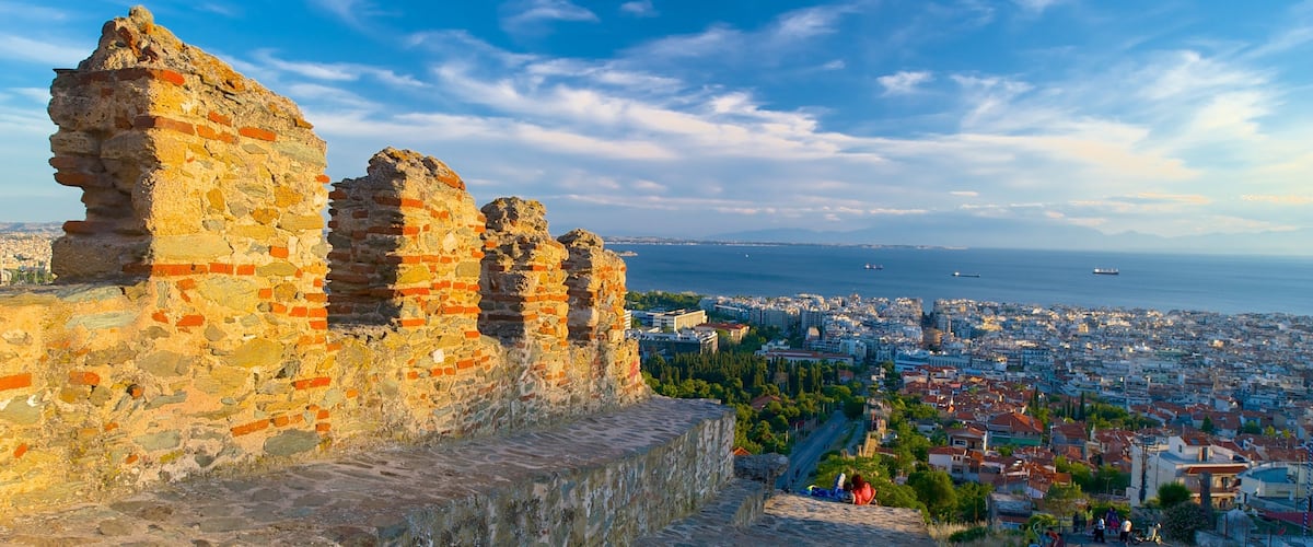 Ancient ruins with a cityscape and the sea in the background.