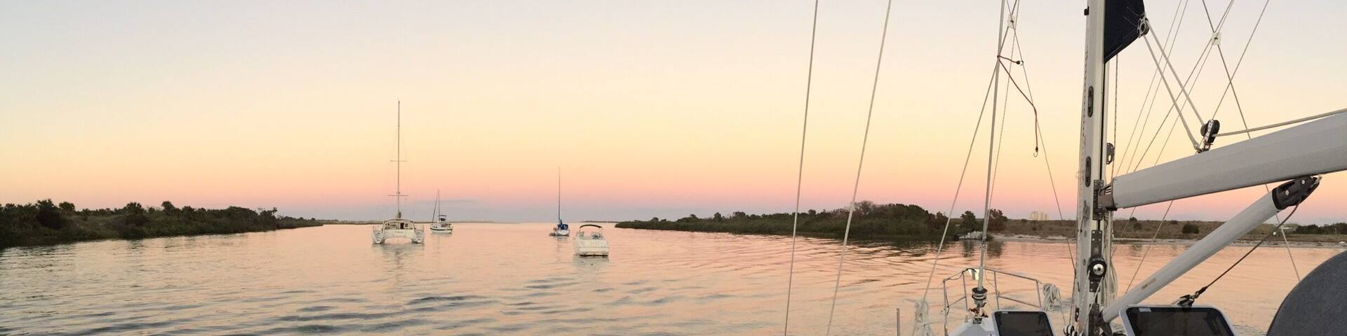 A calm body of water with several sailboats at sunset.