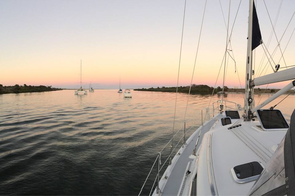 Água calma com vários veleiros ao pôr do sol.