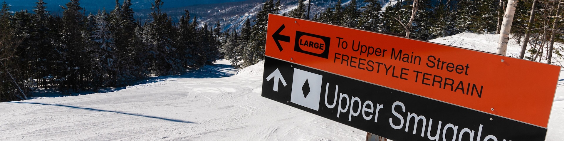 Eine verschneite Berglandschaft mit einem Schild, das Wegweiser zu Upper Main Street und Upper Smugglers zeigt.