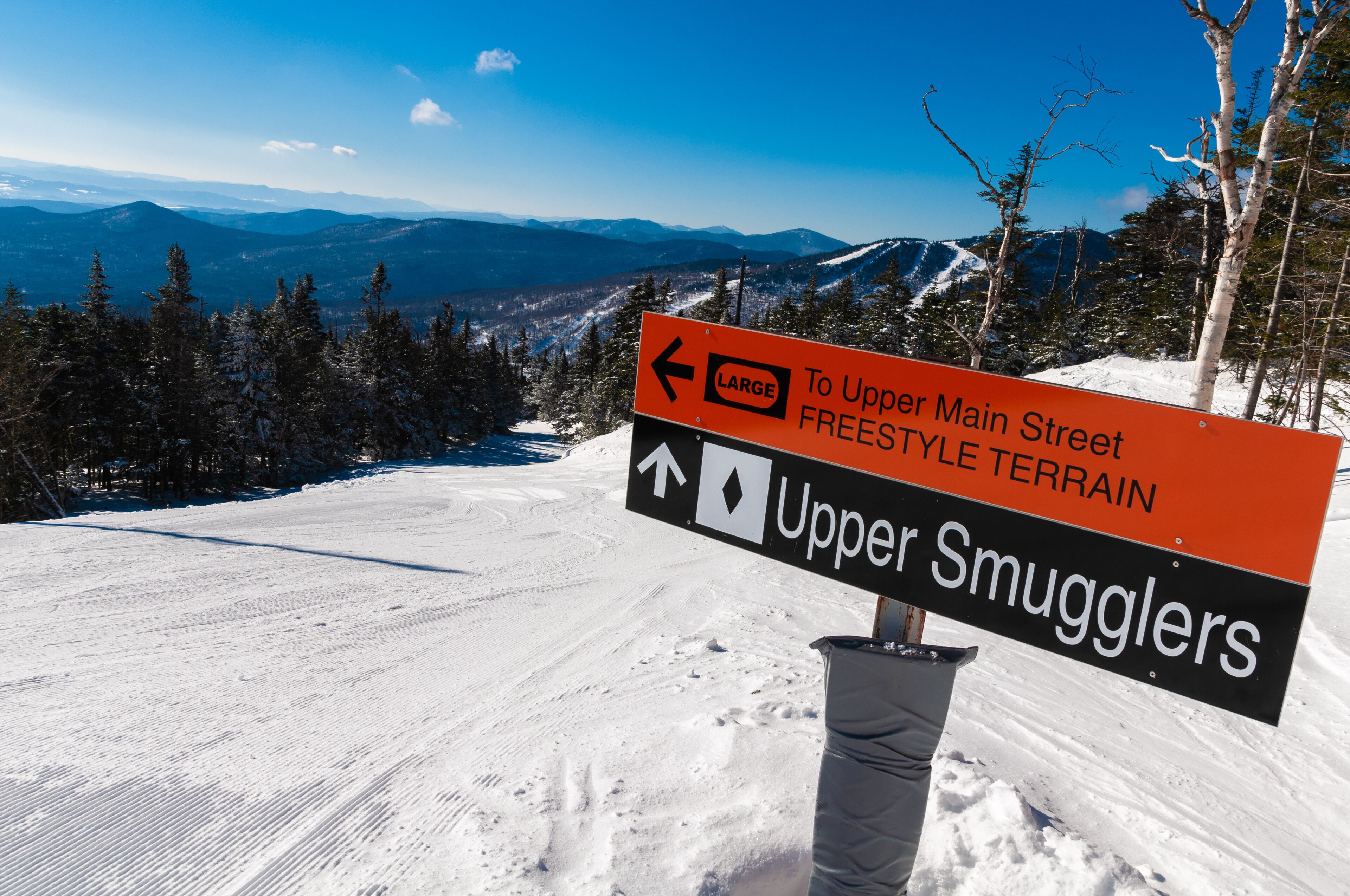 A snowy mountain landscape with a sign indicating directions to Upper Main Street and Upper Smugglers.