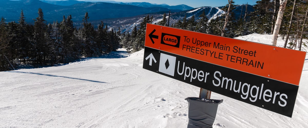 A snowy mountain landscape with a sign indicating directions to Upper Main Street and Upper Smugglers.